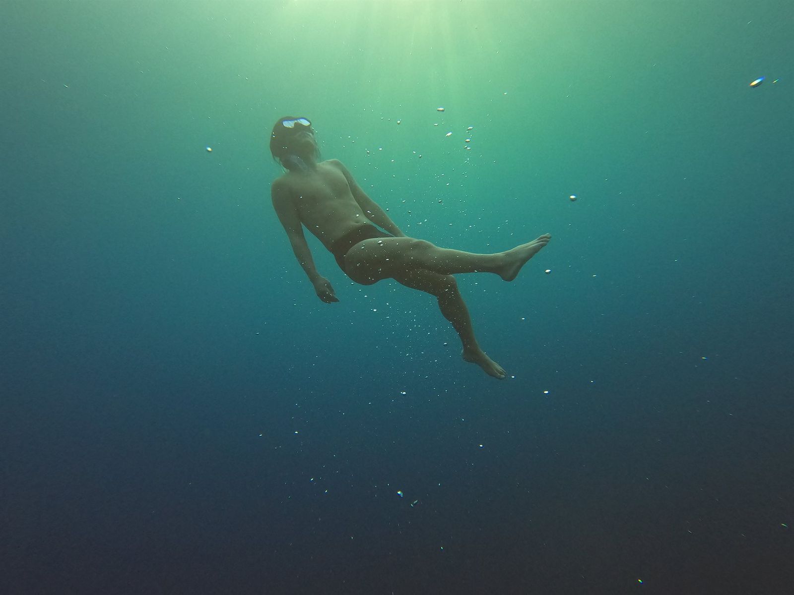 Freediver floating weightless underwater, fully relaxed, as sunlight filters down from the surface